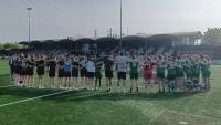 Eine große Gruppe von Sportlern steht in einer Reihe auf einem grünen Sportrasen vor einem Stadiongebäude.