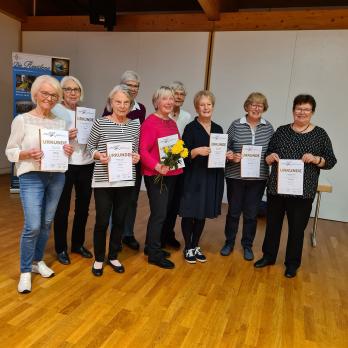 Eine Gruppe von Menschen steht in einer Halle und hält jeweils eine Urkunde in die Kamera.