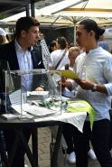 Eine Gruppe von Personen hält an einem Tisch eine Besprechung ab, wobei Männer Dokumente und Unterlagen betrachten.