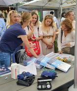 Verschiedene Frauen stehen an einem belebten Marktstand und betrachten Waren auf einem Tisch.