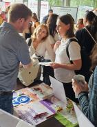 Gruppe von Personen an einem Messe- oder Informationsstand, die Materialien betrachten.