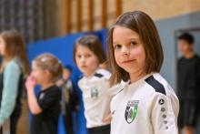 Ein junges Mädchen in einem weißen Sporttrikot steht in einer Sporthalle.