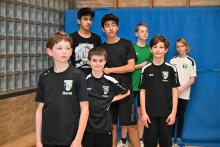 Eine Gruppe von sieben Jungen in schwarzer Sportkleidung posiert als Team in einer Sporthalle.