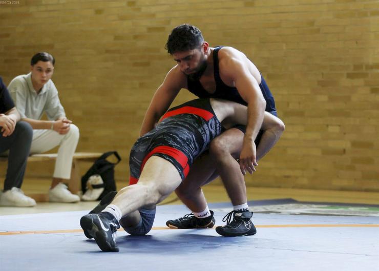 Zwei Männer kämpfen in einem Grappling-Duell auf einer Sportmatte.