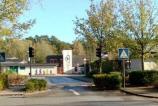 Straßenansicht mit einem Gebäudekomplex und viel Laubwerk im Hintergrund.