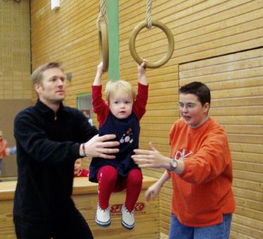 Eine Familie mit einem kleinen Kind und einem Jungen in einer Sporthalle mit Trainingsringen.