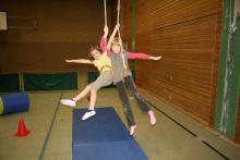Drei Mädchen spielen in einer Halle und schwingen an Seilen.