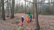 Zwei Personen sammeln in einem Herbstwald Laub und Gegenstände auf dem Boden.