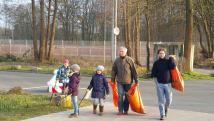 Eine Gruppe von Menschen sammelt in einem Park Müll in großen orangefarbenen Säcken.
