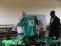 Ein älterer Mann hält in einer Halle ein grünes Fußballtrikot mit der Nummer 10, flankiert von zwei anderen Männern.