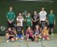Eine Gruppe von Jugendlichen posiert mit Badmintonrackets und sportlicher Kleidung auf einem Indoor-Spielfeld.
