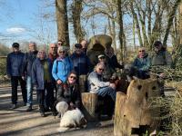 Eine Gruppe von Menschen steht vor einem Waldhintergrund, mit einigen skulpturalen Elementen im Vordergrund.
