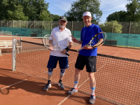 Zwei Männer in Sportkleidung stehen lächelnd auf einem Tennisplatz mit Tennisschlägern.
