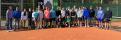 Eine große Gruppe von Menschen, bestehend aus Erwachsenen und Kindern, steht in einer Reihe auf einem roten Spielfeldrand.