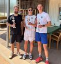 Drei junge Männer in sportlicher Kleidung stehen zusammen vor einem Außenbereich.