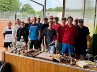 Eine Gruppe von Männern mit Trophäen vor einem Fenster, das einen Tennisplatz zeigt.