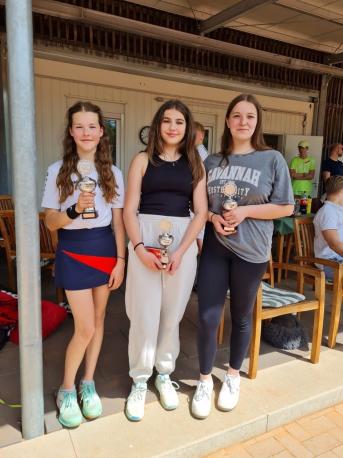 Vier lächelnde Teenagerinnen stehen draußen vor einem Gebäude und posieren für ein Gruppenfoto.