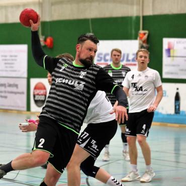 Ein Handballspieler in gestreiftem Trikot wirft einen roten Ball in einem Sporthallen-Spiel.