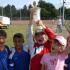Mehrere Jungen stehen auf einem Sportplatz und halten gemeinsam einen großen Pokal, was auf einen sportlichen Sieg hindeutet.