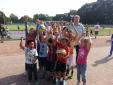 Eine große Gruppe von Kindern und Jugendlichen posiert für ein Gruppenfoto auf einem gepflasterten Sportplatz im Freien.