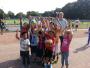 Eine große Gruppe von Kindern und Jugendlichen posiert für ein Gruppenfoto auf einem gepflasterten Sportplatz im Freien.