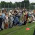 Eine große Menschenmenge beobachtet einen Sportwettkampf hinter einem Seil auf einem Rasenfeld.