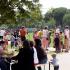 Eine große Gruppe von Menschen, darunter Familien und Kinder, versammelt sich bei einem Treffen in einem grünen Park.