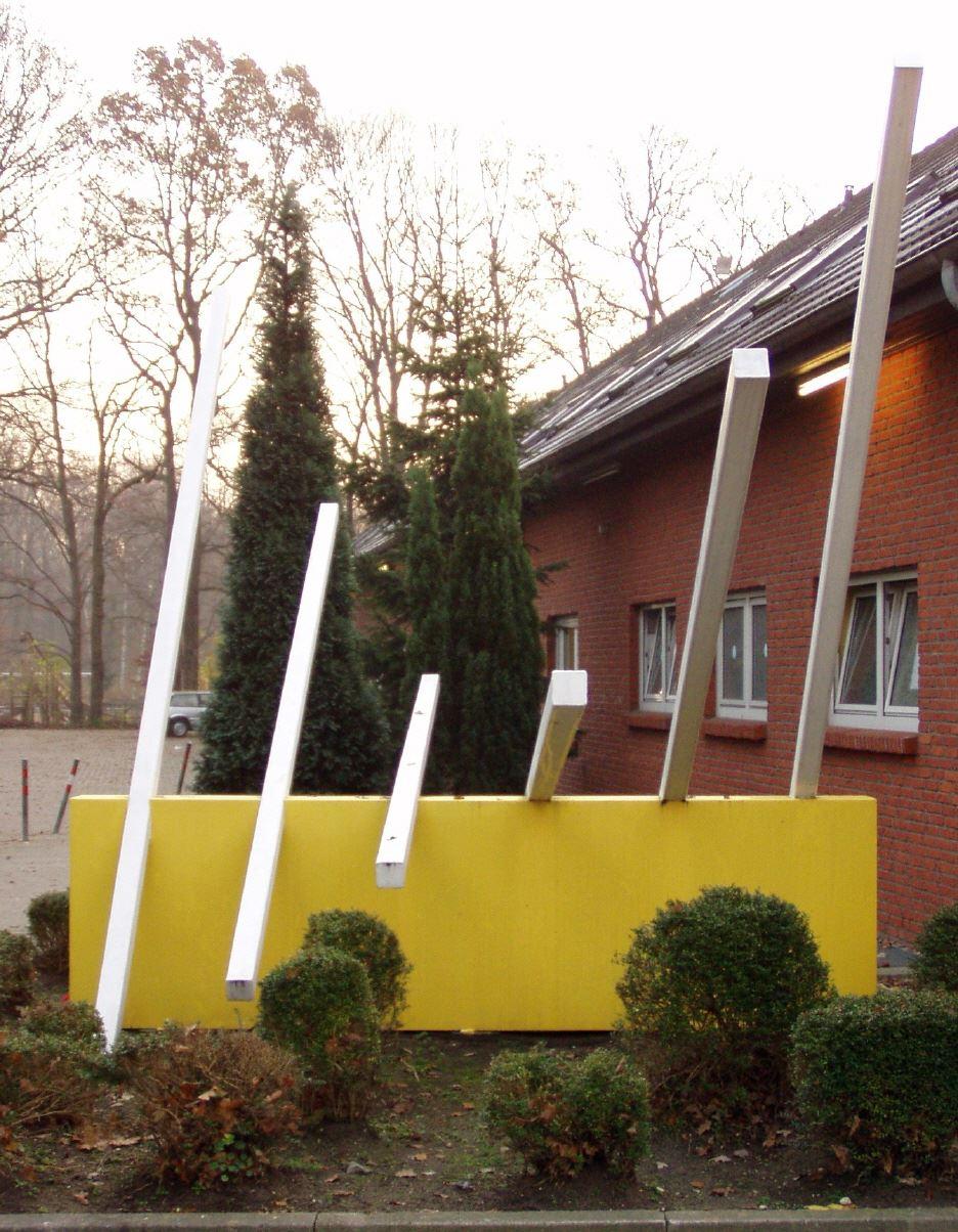 Die Fassade eines Backsteingebäudes mit einem leuchtend gelben Blumenkasten im Vordergrund, akzentuiert durch weiße vertikale Stützen.