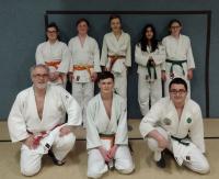 Eine Gruppe von Personen in Kampfsport-Unis, die in einem Dojo für ein Gruppenfoto posieren.