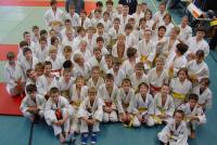 Eine große Gruppe von Kindern, die in hellen Uniformen auf einem Sporthallenboden für ein Gruppenfoto posieren.