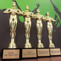 Fünf goldfarbene Trophäen, die sportliche Auszeichnungen darstellen, stehen nebeneinander, darunter sind Plaketten mit Jahresangaben angebracht.
