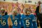 Eine Gruppe jubelnder junger Sportlerinnen mit blauen Trikots in einer Sporthalle.