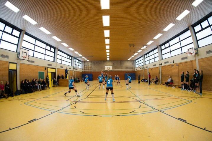 Ein großer, gut beleuchteter Sporthallenboden mit Markierungen, auf dem mehrere Personen bei einer Sportveranstaltung stehen.