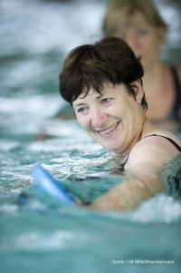 Eine lächelnde Frau im Wasser, die sich in einem Schwimmbecken befindet.