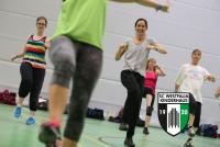 Gruppe von Erwachsenen, die in einer Sporthalle an einem Fitnesskurs teilnehmen.