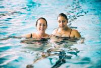 Zwei Frauen stehen lächelnd im flachen, blauen Wasser.