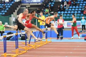 Mehrere männliche Athleten rennen während eines Sprintwettkampfs auf einer Tartanbahn in einer Sportarena.