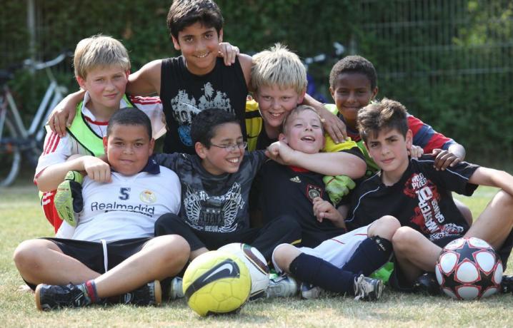 Eine große Gruppe von Jungen steht draußen auf einem Sportrasen und posiert mit mehreren Fußballen.