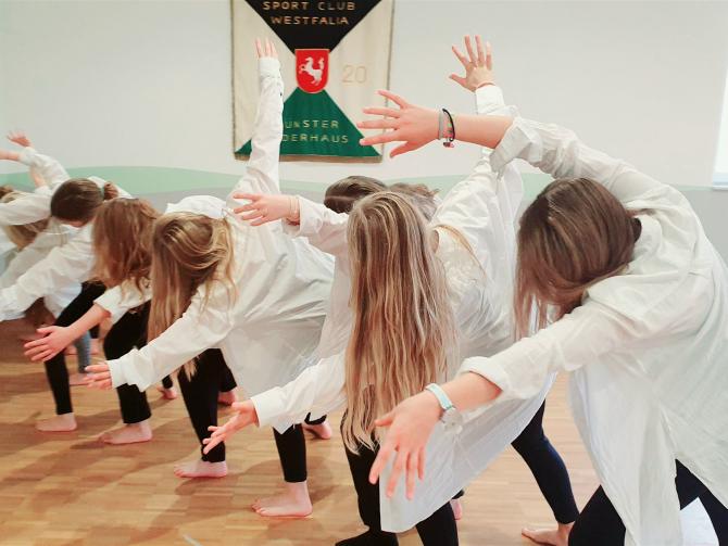 Eine Gruppe von Personen führt in einer Turnhalle ein gemeinsames Fitness- oder Tanztraining durch.