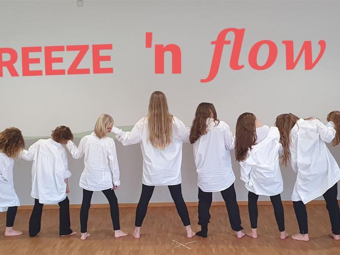 Eine Gruppe von Menschen, die in einer Reihe posieren und verschiedene Posen einnehmen, vor einem Hintergrund mit dem Schriftzug Freeze n flow.