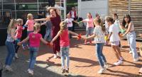 Viele Kinder und Jugendliche tanzen und spielen ausgelassen auf einem Platz im Freien, überwacht von Erwachsenen.