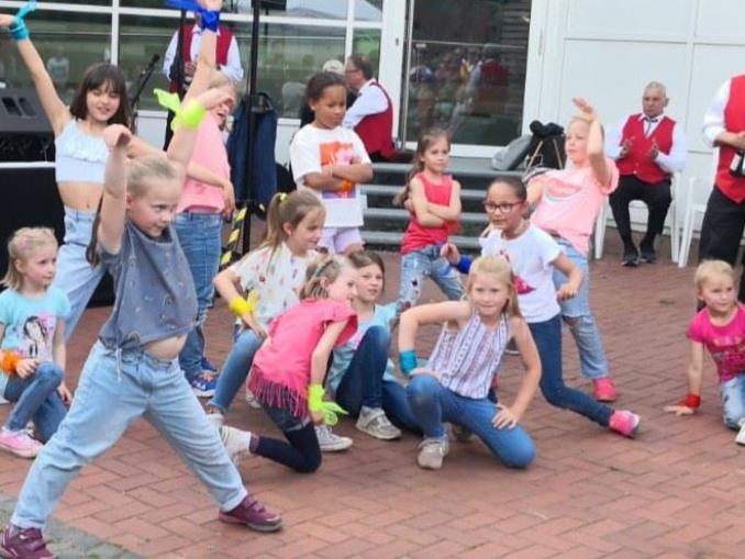 Eine Gruppe von Kindern unterschiedlichen Alters, die freudig im Freien auf einem gefliesten Boden posieren.