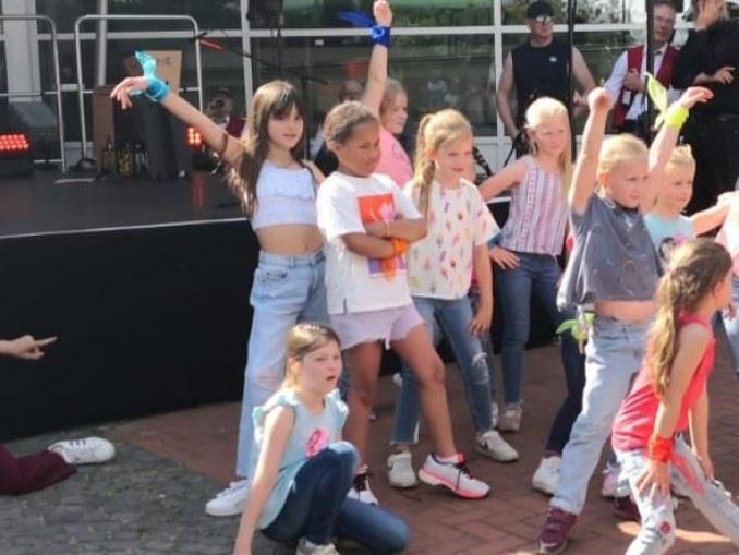 Gruppe von Kindern verschiedener Alters, die im Freien vor einer dunklen Bühne posieren.