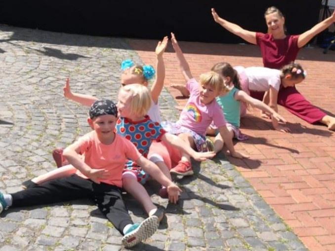 Eine Gruppe spielender Kinder und eine erwachsene Frau sind im Freien auf Pflastersteinen zu sehen.