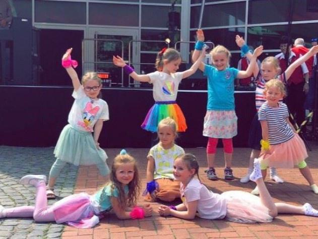 Eine Gruppe von Kindern in bunten Kostümen posieren und lächeln während einer Gruppenaufführung.