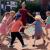 Eine Gruppe von Erwachsenen und Kindern spielt draußen auf einem gepflasterten Platz.