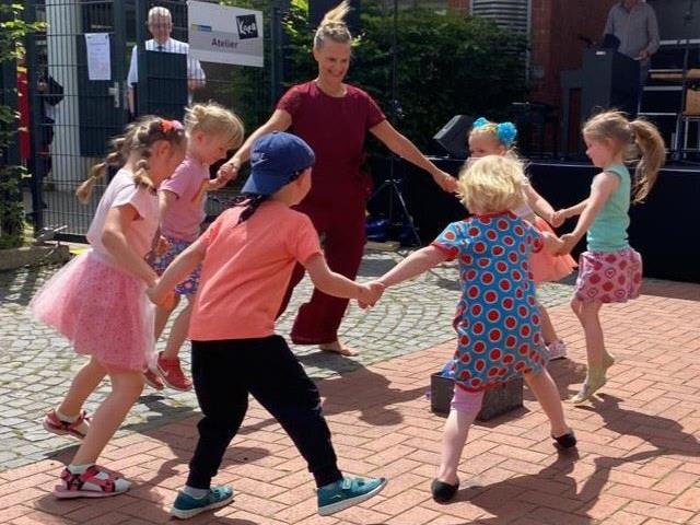 Eine Gruppe von Erwachsenen und Kindern spielt draußen auf einem gepflasterten Platz.