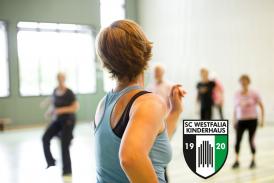Eine Sportlerin steht im Vordergrund und blickt in eine Gruppe von Personen, die sich in einer großen Sporthalle befinden.