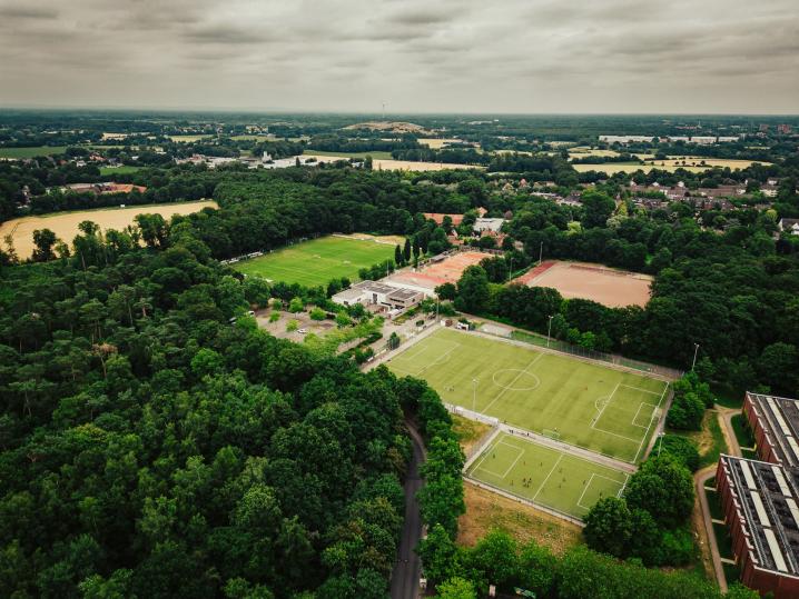 Luftaufnahme von Sportplätzen und Wald inmitten einer städtischen Landschaft.